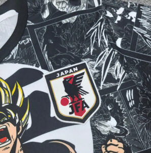 D5ABBC50-E540-488C-A88C-AE9C69526AA9 | UAE SPORT STORE Close-up of a Japan Football Association emblem on a black-and-white manga-themed jersey, with bold panels in the background.