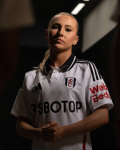 D9gtiXlMUu93vVQ | UAE SPORT STORE Portrait of a female soccer player in a white jersey with black trim, hands clasped in front and a confident expression.