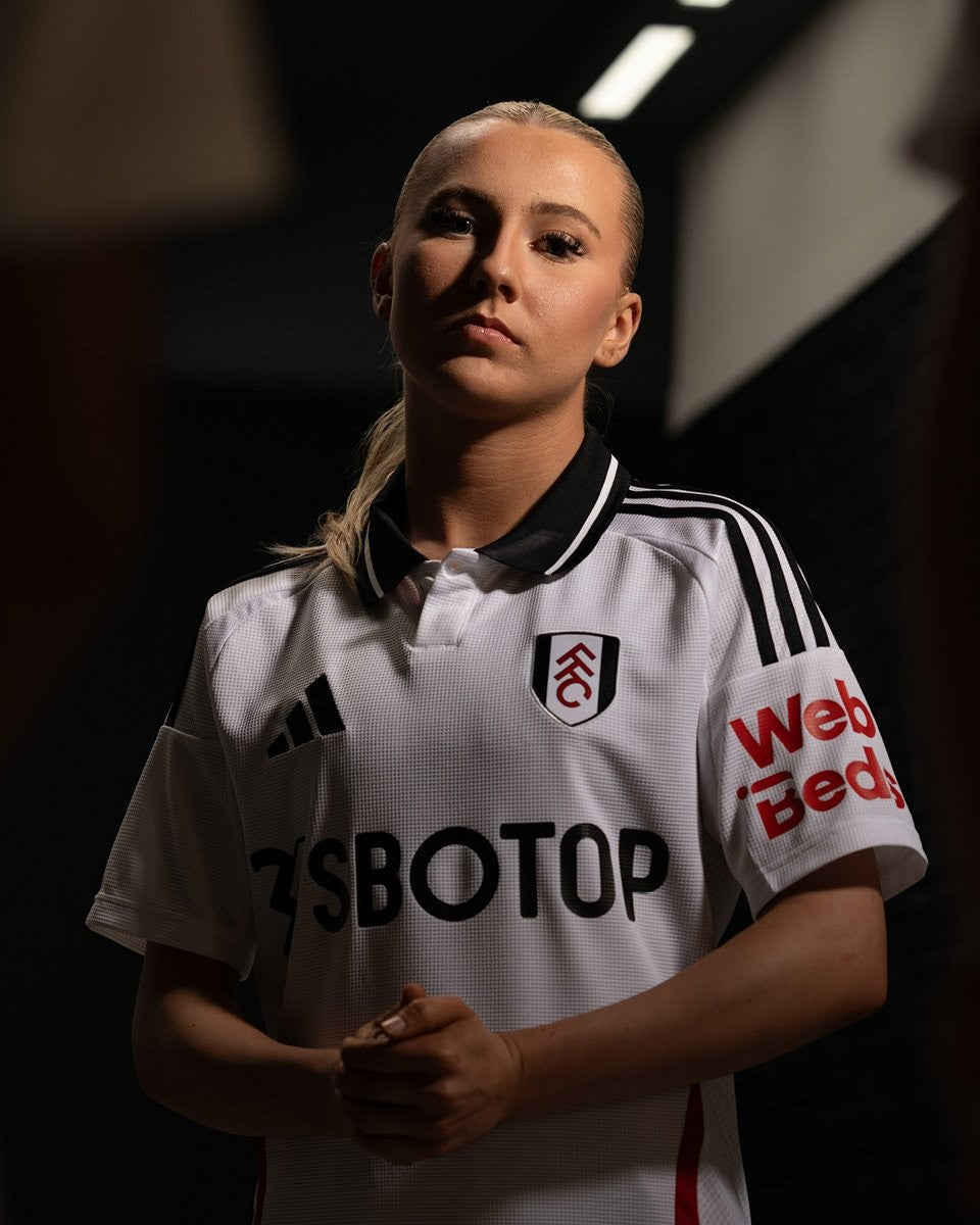 D9gtiXlMUu93vVQ | UAE SPORT STORE Portrait of a female soccer player in a white jersey with black trim, hands clasped in front and a confident expression.
