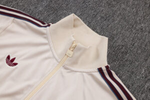 Cream-colored track jacket with a beige zipper, maroon stripes along the sleeves, and a burgundy trefoil logo on the chest.
