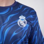 Blue Real Madrid football jersey with wavy pattern and white club crest on the chest.