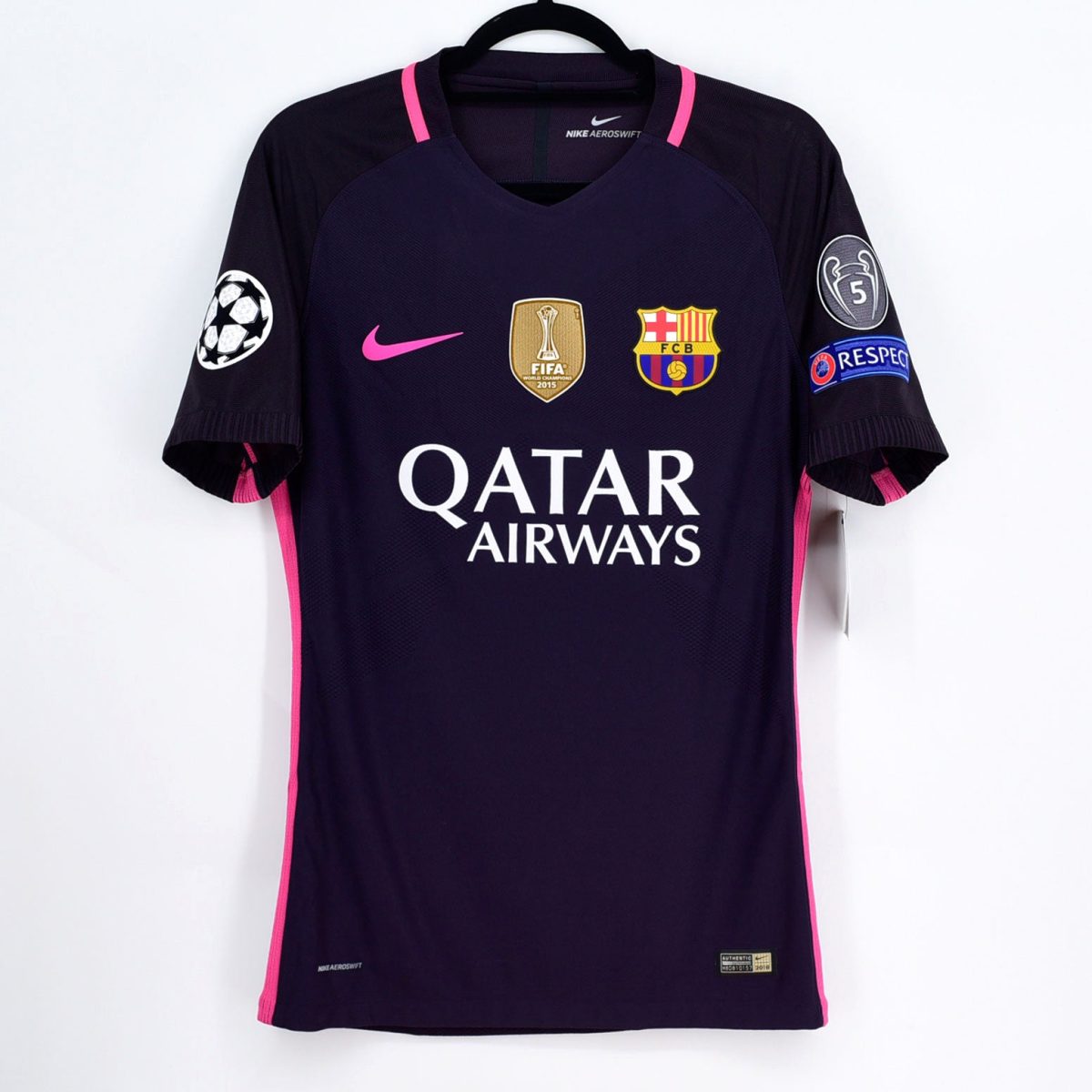 Dark blue FC Barcelona soccer jersey with pink accents on a hanger, featuring Qatar Airways sponsor text, Nike swoosh, Barca crest, and UEFA/Champions League patches on the sleeves.