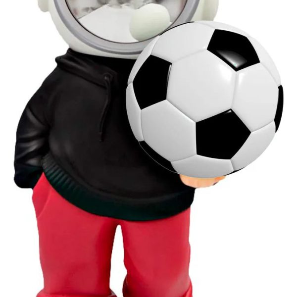 Plastic astronaut figurine with a shiny round helmet, holding a soccer ball against a white background, wearing red pants and black shoes.
