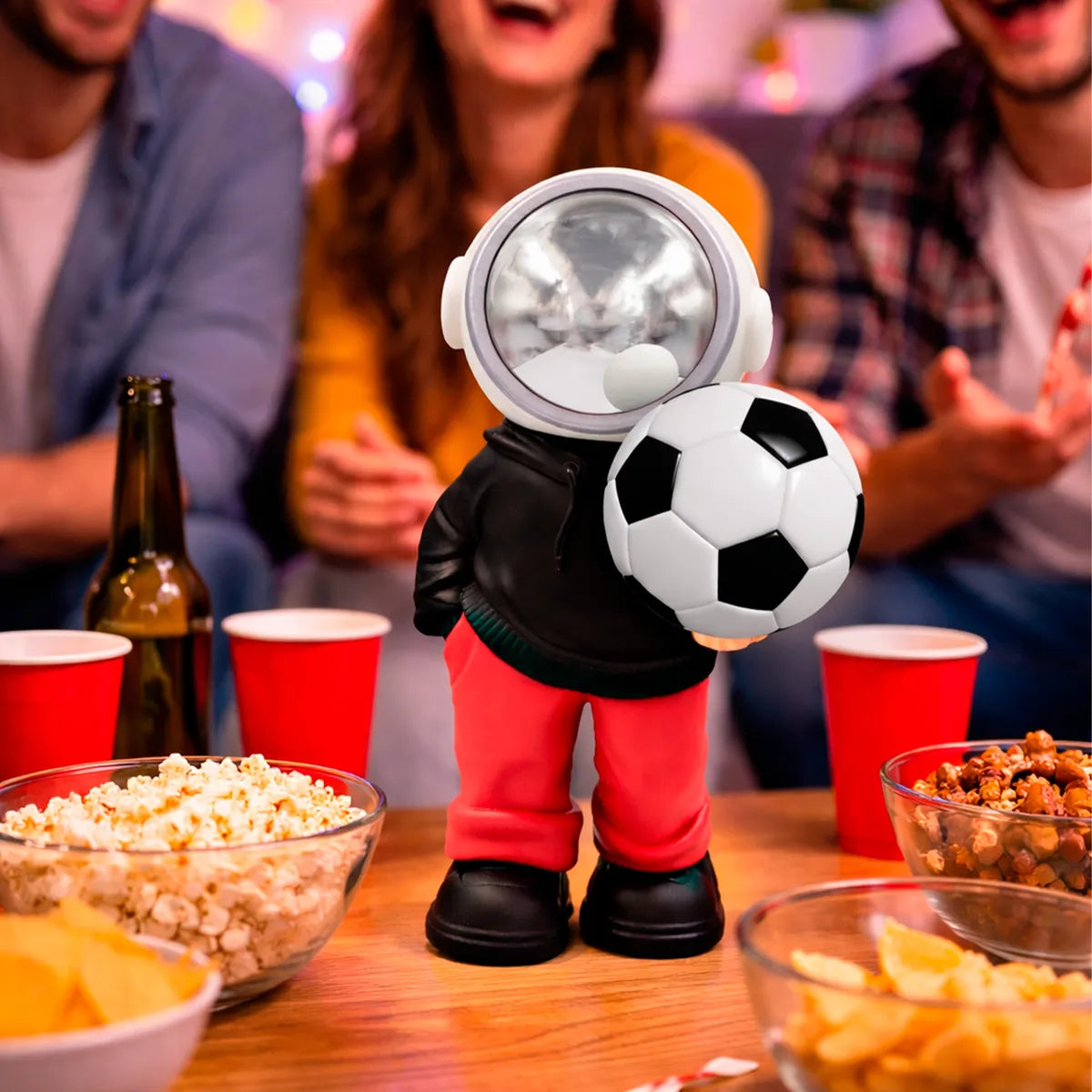 D_NQ_NP_2X_885849-MLM105765684125_012026-F-bocina-lampara-led-inalambrica-astronauta-balon-futbol | UAE SPORT STORE Plastic astronaut figure in a black jacket and red pants, holding a soccer ball at a party table.