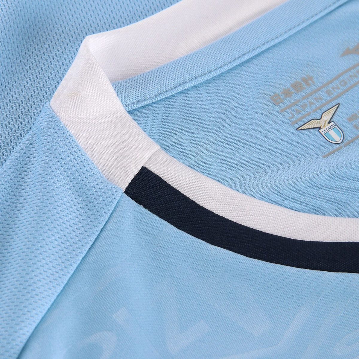 Close-up of a light blue soccer jersey collar with white trim and a navy stripe, featuring a Lazio crest.