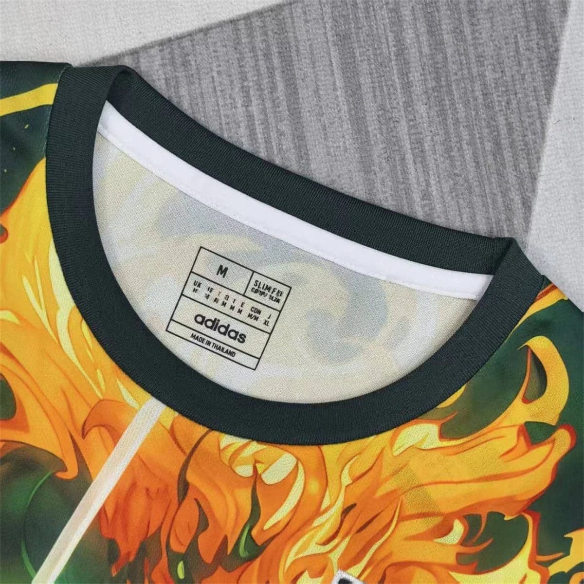 Close-up of a colorful flame-pattern Adidas shirt collar with a size tag reading 'M' and 'Made in Thailand'.