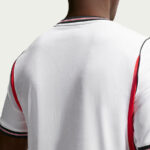 Back view of a white athletic jersey with red and black trim along sleeves and collar.