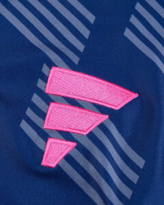 Close-up of a bright pink embroidered emblem on blue athletic fabric with diagonal gray stripes.