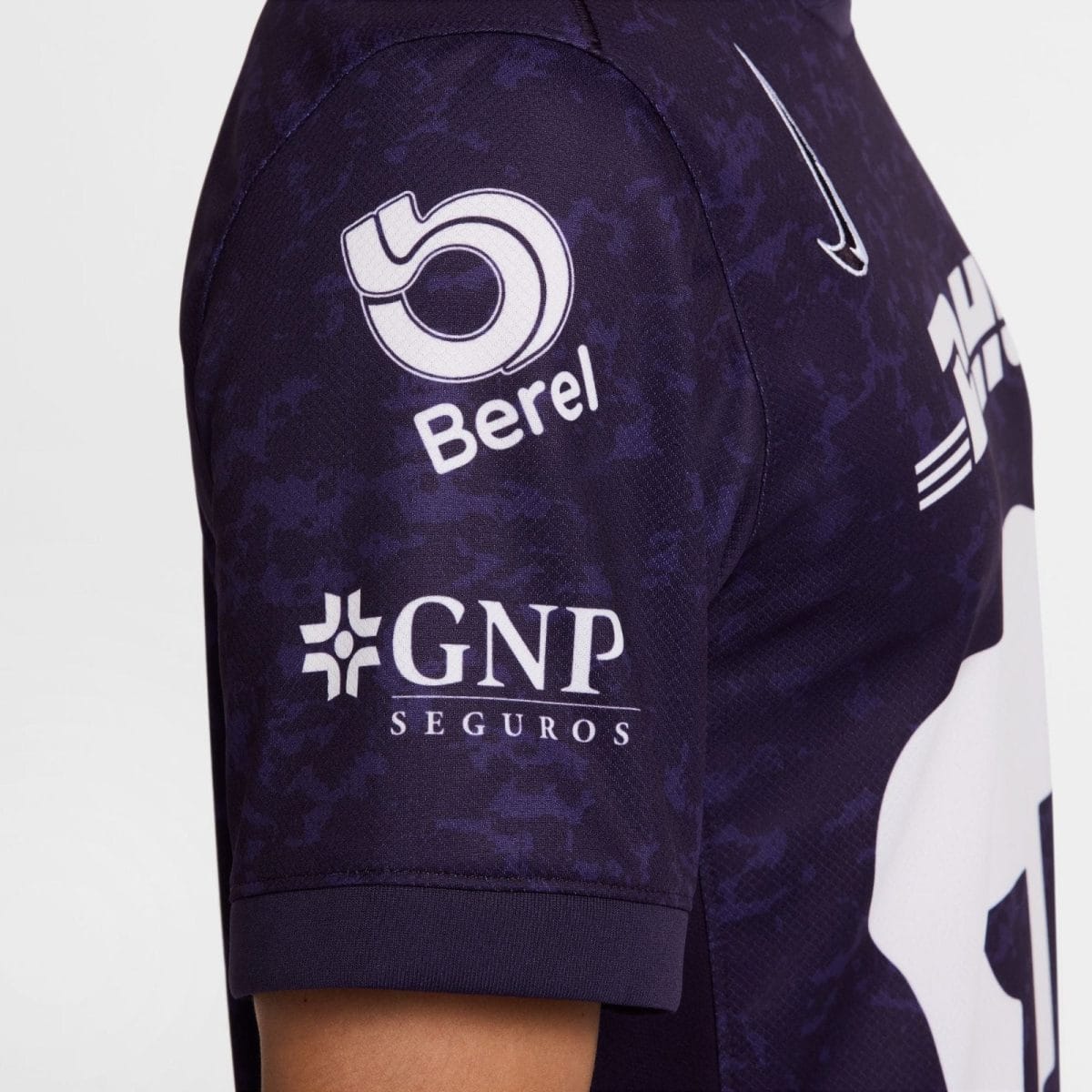 Close-up of a dark purple sports jersey sleeve showing sponsor logos, including 'Borel' circular emblem and 'GNP Seguros' text with a partial Nike swoosh nearby.