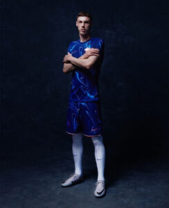 Athlete posing in a blue patterned sports jersey and shorts, arms crossed, against a dark studio backdrop.