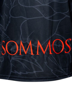 Dark navy fabric with a subtle floral pattern and bold red text reading 'SOMMOS' along the bottom edge.
