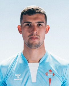 Close-up portrait of a man with short dark hair wearing a light blue sports jersey with a crest on the left chest, neutral expression.