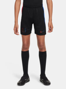 Person wearing black soccer shorts with red and blue side stripes, crest on the left leg and a Nike swoosh on the right, paired with black socks and cleats.