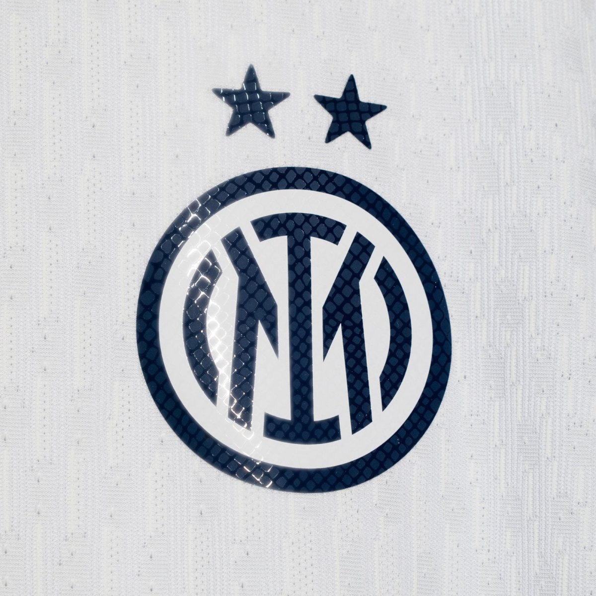 Close-up of a dark blue VW circular logo with two stars above on a light textured surface.