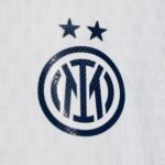 Close-up of a dark blue VW circular logo with two stars above on a light textured surface.