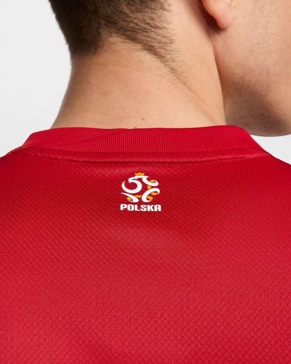 Back view of a person wearing a red sports jersey with the Poland (Polska) crest on the upper back near the collar
