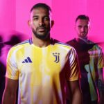 Two men in yellow Juventus jerseys stand against a bright pink background, foreground man with a beard looking at the camera.