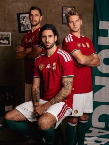 Three male soccer players in red Hungary jerseys pose in a studio setting, arms crossed or resting, looking at the camera.