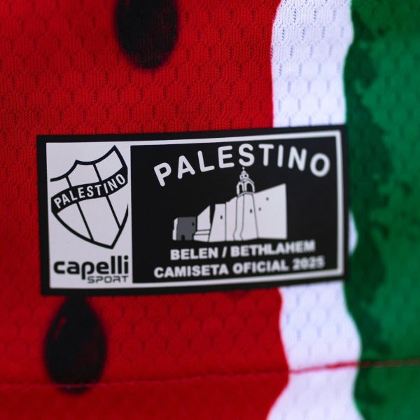 Close-up of a PALESTINO jersey tag on red-white-green fabric, reading 'Belen/Bethlehem Camiseta Oficial 2025'.