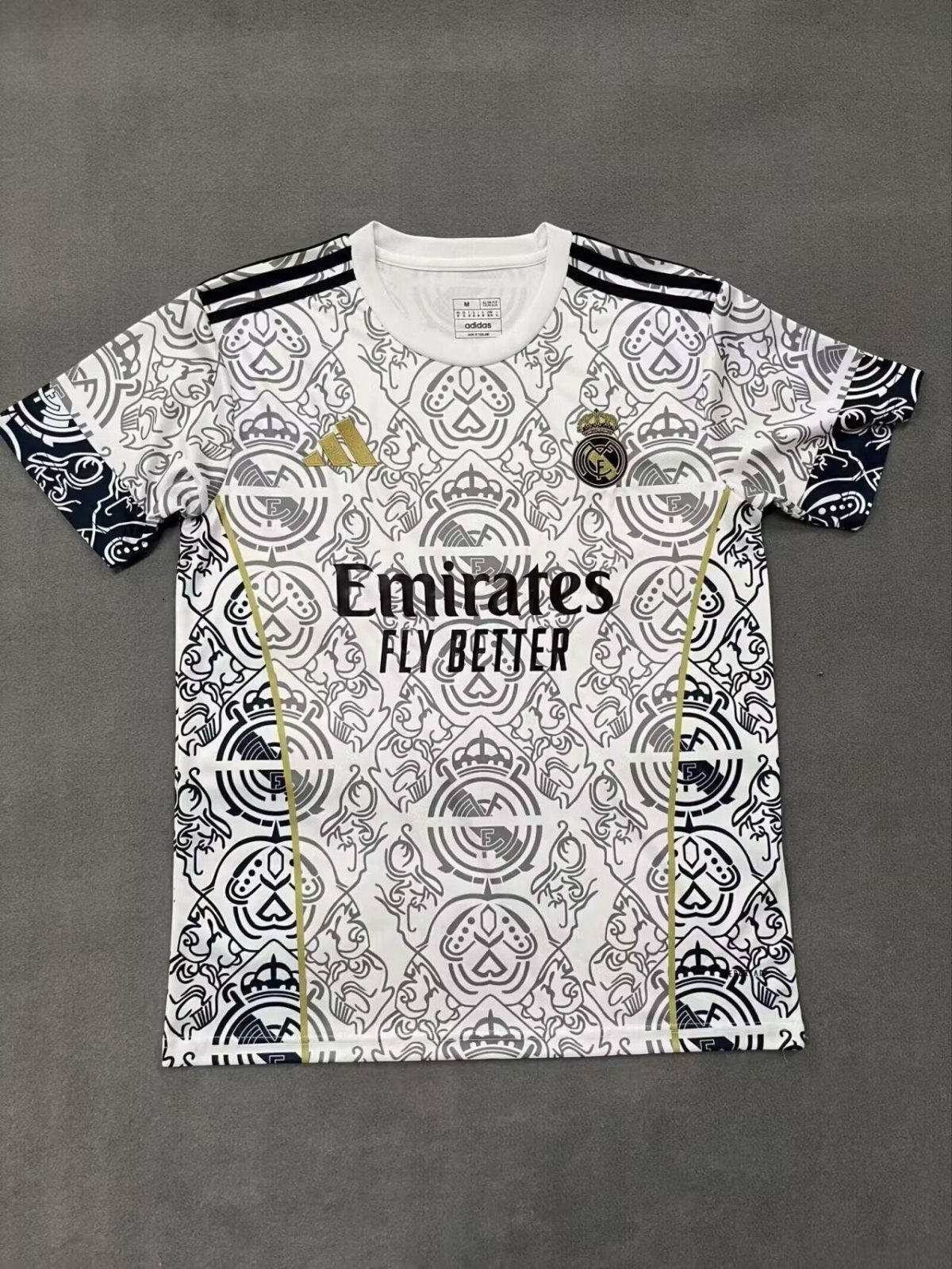 White Real Madrid football jersey with an intricate gray pattern, Real Madrid crest, Adidas logo, and Emirates Fly Better sponsor text across the chest.