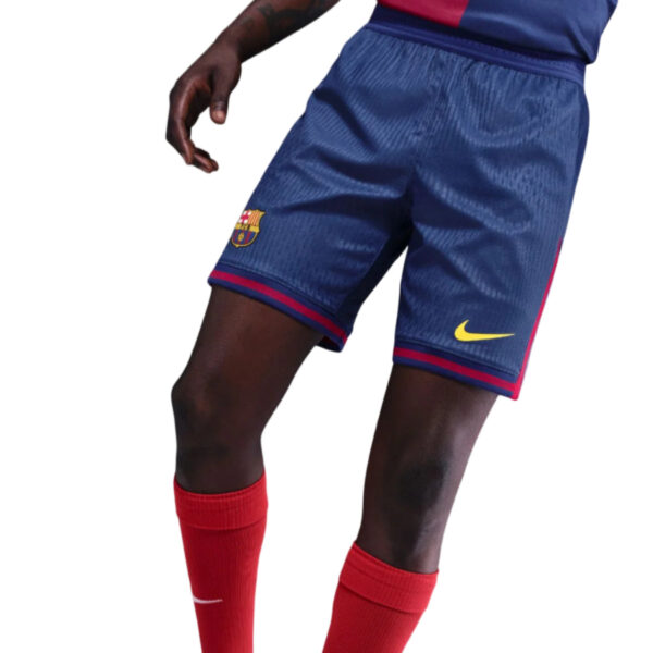 Partial view of a soccer player wearing blue Barcelona shorts with the club crest and a yellow Nike swoosh, and red socks.