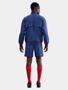 Back view of a person in a blue athletic jacket and matching shorts with red trim and red socks from behind.