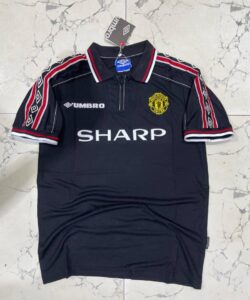 Dark Manchester United jersey on hanger featuring crest, Umbro logo, and 'SHARP' sponsor; navy with red-white trim.