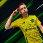 GbUVpzmo54A957y | UAE SPORT STORE Young soccer player in a yellow Celtic FC jersey saluting with his right hand against a dark green background.