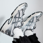 Two silver-gray running shoes with patterned soles, feet crossed in the air against a light background.