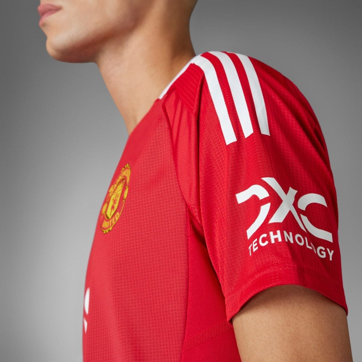Close-up of a red Manchester United jersey with white shoulder stripes and the club crest.