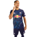 Male model in a navy blue football jersey with Red Bull sponsor and a wavy pattern, touching his ear.