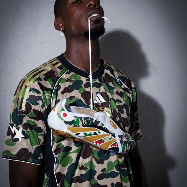 Portrait of a man in a camo shirt with a white sneaker strapped across his chest and laces hanging from his mouth.