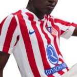 Close-up of a person wearing a red-and-white striped soccer jersey with a blue Nike swoosh and Riyadh Air logo on the chest.