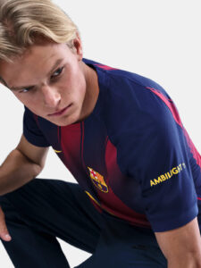 Young man in a FC Barcelona jersey leaning forward and looking to the left, torso and face visible