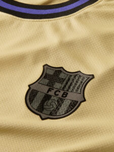 HJ4603-784_431735711_D_P_1X1_bd5bdcc4-ba8a-4027-91f3-6555c6b1427b | UAE SPORT STORE Close-up of a gold jersey fabric with the FC Barcelona (FCB) shield emblem displayed.