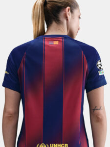 Back view of a person wearing a blue and red striped soccer jersey, with a small flag at the neck and a UNHCR logo near the bottom hem.