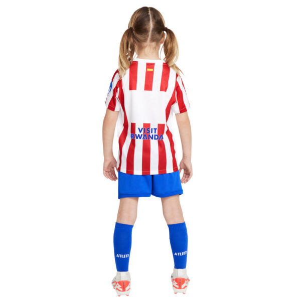 Child in red-and-white striped soccer jersey with blue shorts, seen from behind; jersey reads 'VISIT RWANDA' on the back.