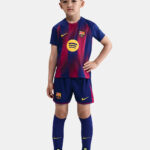 Young boy models a FC Barcelona youth soccer kit with blue‑red striped shirt, shorts, and neon yellow cleats.