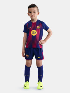 Young boy models a FC Barcelona youth soccer kit with blue‑red striped shirt, shorts, and neon yellow cleats.