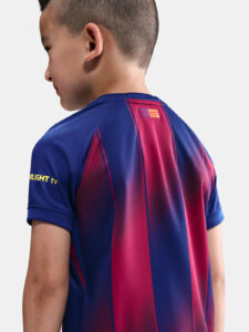 Back view of a child wearing a blue and maroon striped sports jersey, with a small flag patch on the upper back and yellow text on the left sleeve.