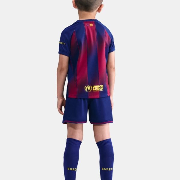 Boy wearing a Barcelona football kit seen from the back, blue and red striped jersey with UNHCR logo and blue shorts.