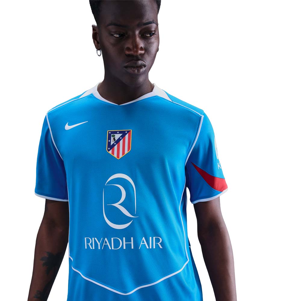 HM3200-407_1 Person wearing a bright blue soccer jersey with Riyadh Air logo and an Atletico Madrid crest on the chest, white trim visible at collar and sleeves.