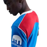 Person wearing a blue and red Kraken jersey, shown from the side, with the Kraken logo on the sleeve visible.
