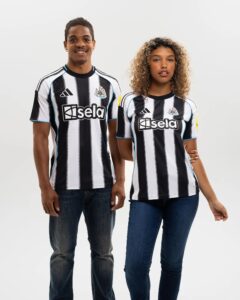 Two people wearing black-and-white striped Newcastle United football jerseys stand side by side against a plain white background, smiling slightly.