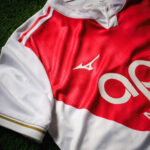 Red and white sports jersey laid on green grass, showing a white Mizuno logo and large partial number on the front.