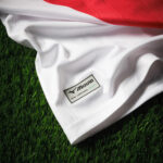 White Mizuno jersey on artificial grass with a small official licensed product tag visible on the fabric edge.