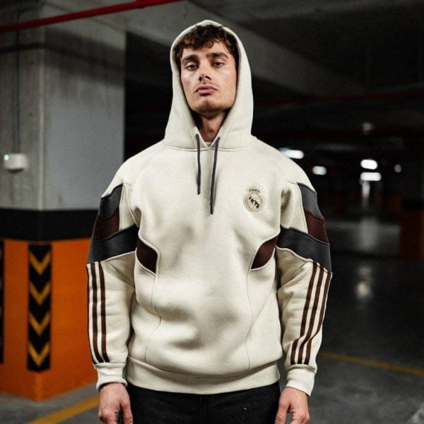 Young man wearing a cream hoodie with dark brown panels stands in a dim underground parking garage.