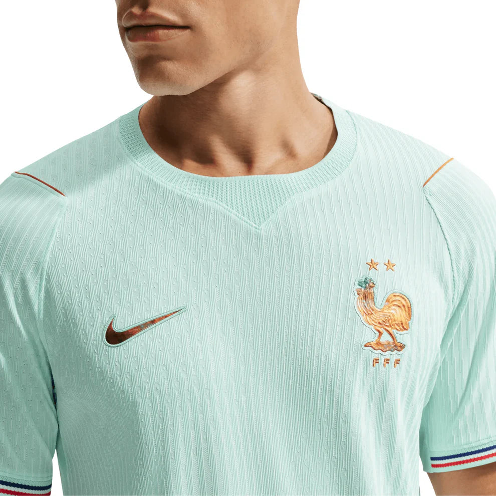 IB5200-394_3 | UAE SPORT STORE Close-up of a light turquoise France national team soccer jersey, featuring a gold Nike swoosh and the FFF rooster crest with two stars on the chest.