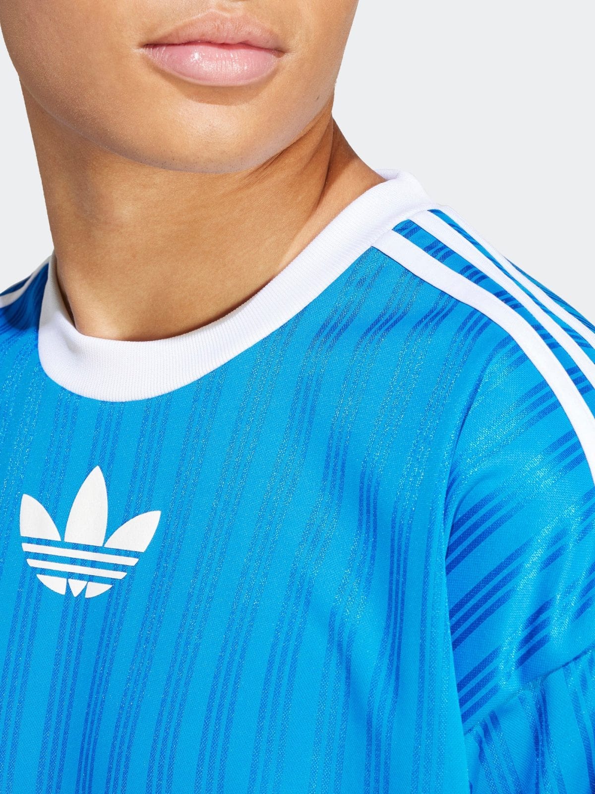 Close-up of a person’s lower face and neck wearing a blue Adidas jersey with a white trefoil logo.