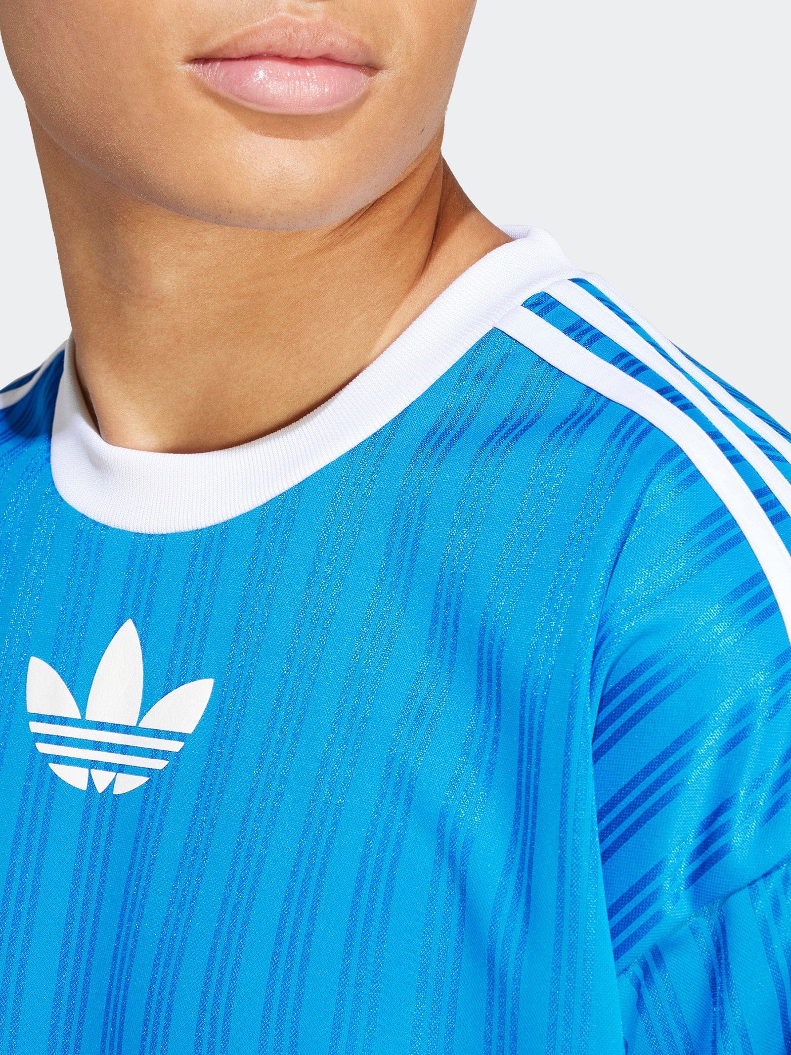 IM9456_7_APPAREL_OnModel_DetailView1_grey_2048x_93321b23-6a04-491f-b5be-0cf755210ef4 | UAE SPORT STORE Close-up of a person’s lower face and neck wearing a blue Adidas jersey with a white trefoil logo.